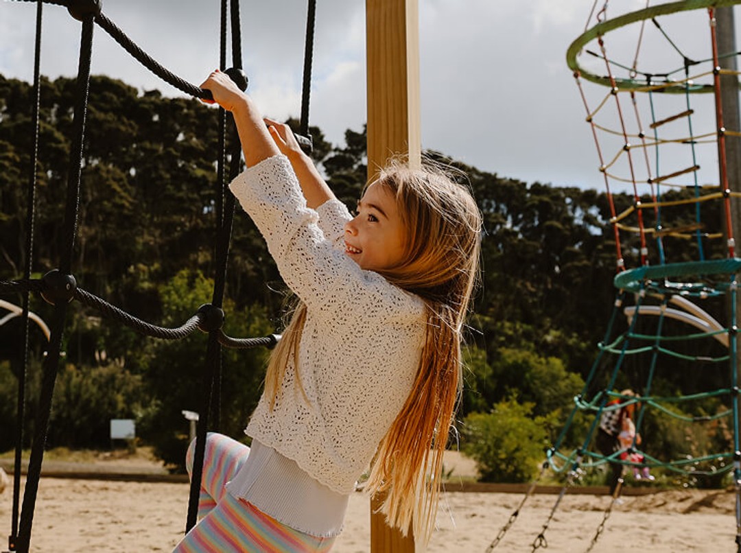 Girl in white cardigan climbing rope structure in playground