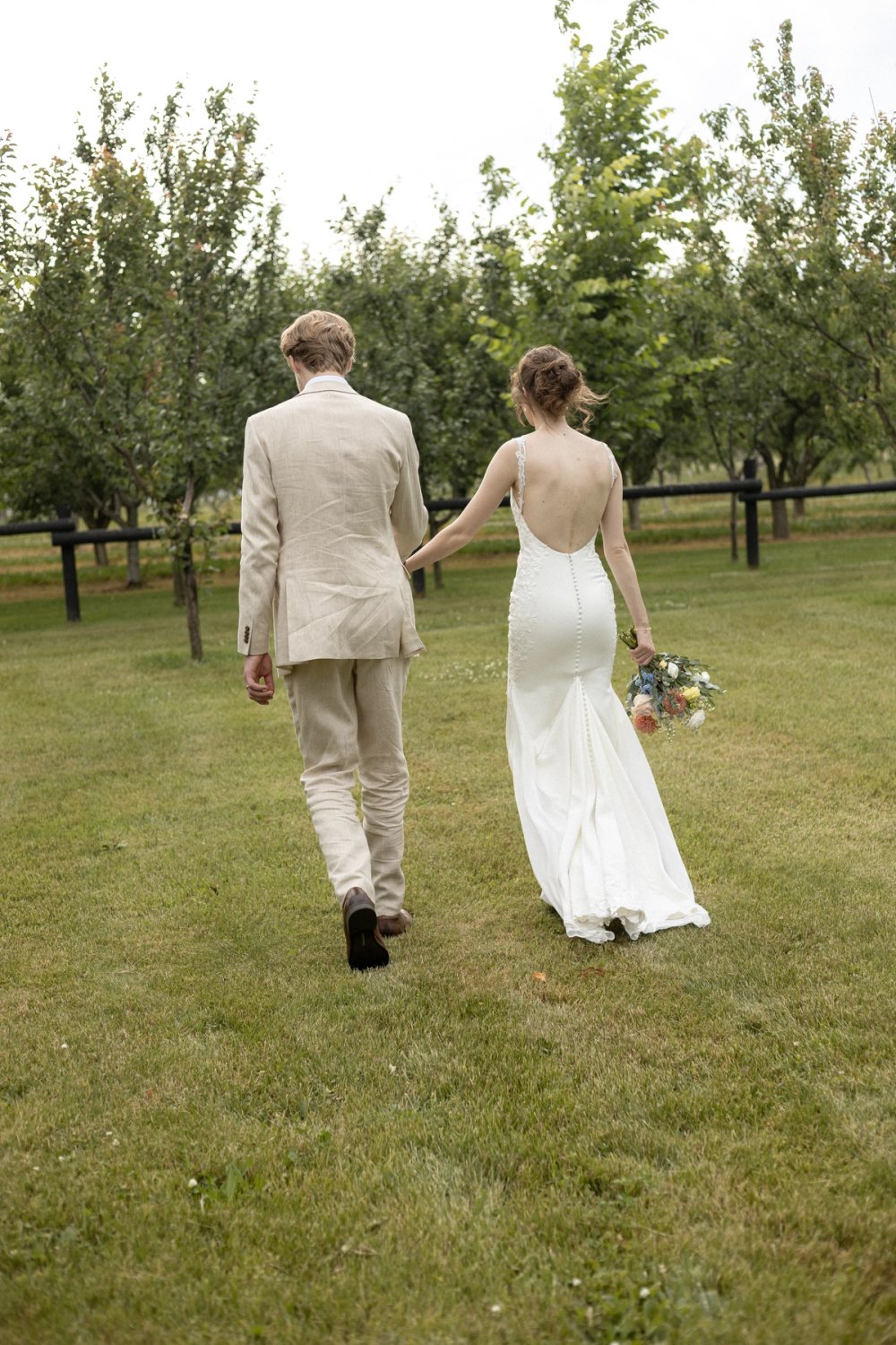 Bride and groom walk toward orchard trees