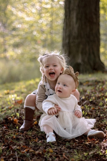 toddler hugging baby sister from behind smiling with joy - Family Photography