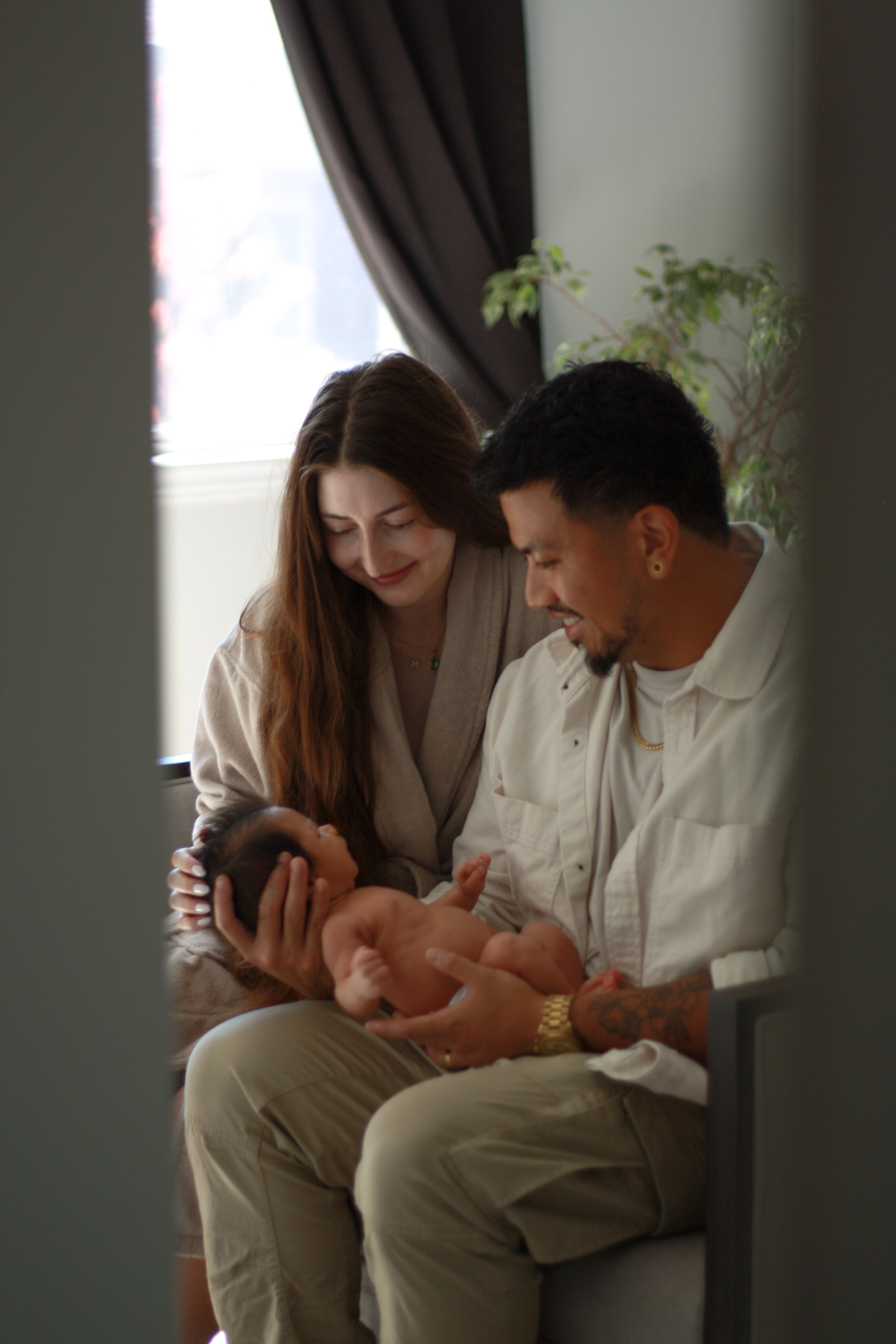 Couple sitting on bench at end of bed holding newborn baby looking lovingly - Newborn photography