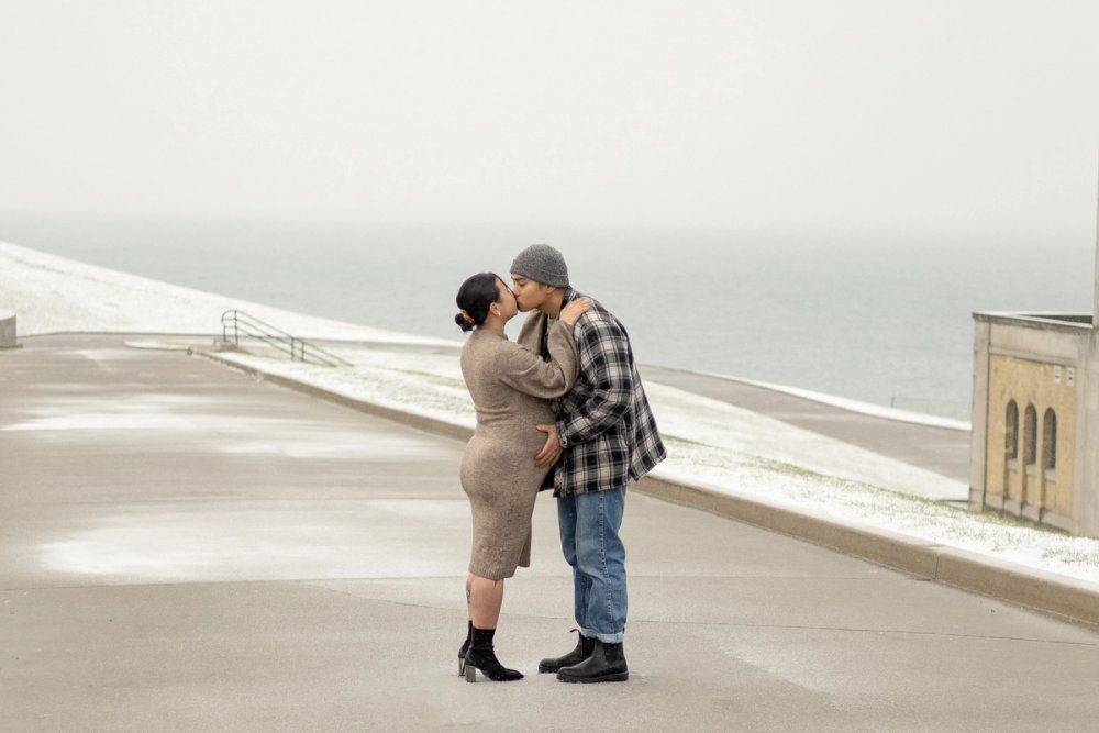 Pregnant mother and expecting father kissing against the iconic lakeside view at the R.C. Harris Water Treatment Plant. -Newmarket Maternity Photography
