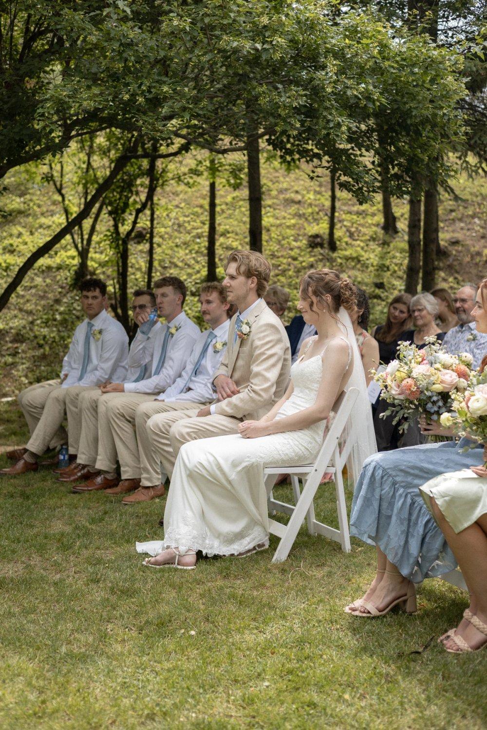wedding party seated during during outdoor wedding ceremony surrounded by trees