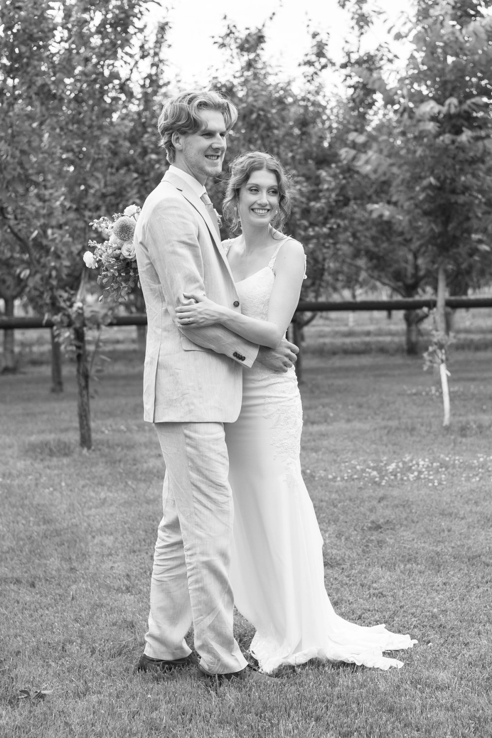Bride and groom sharing embrace near orchard trees