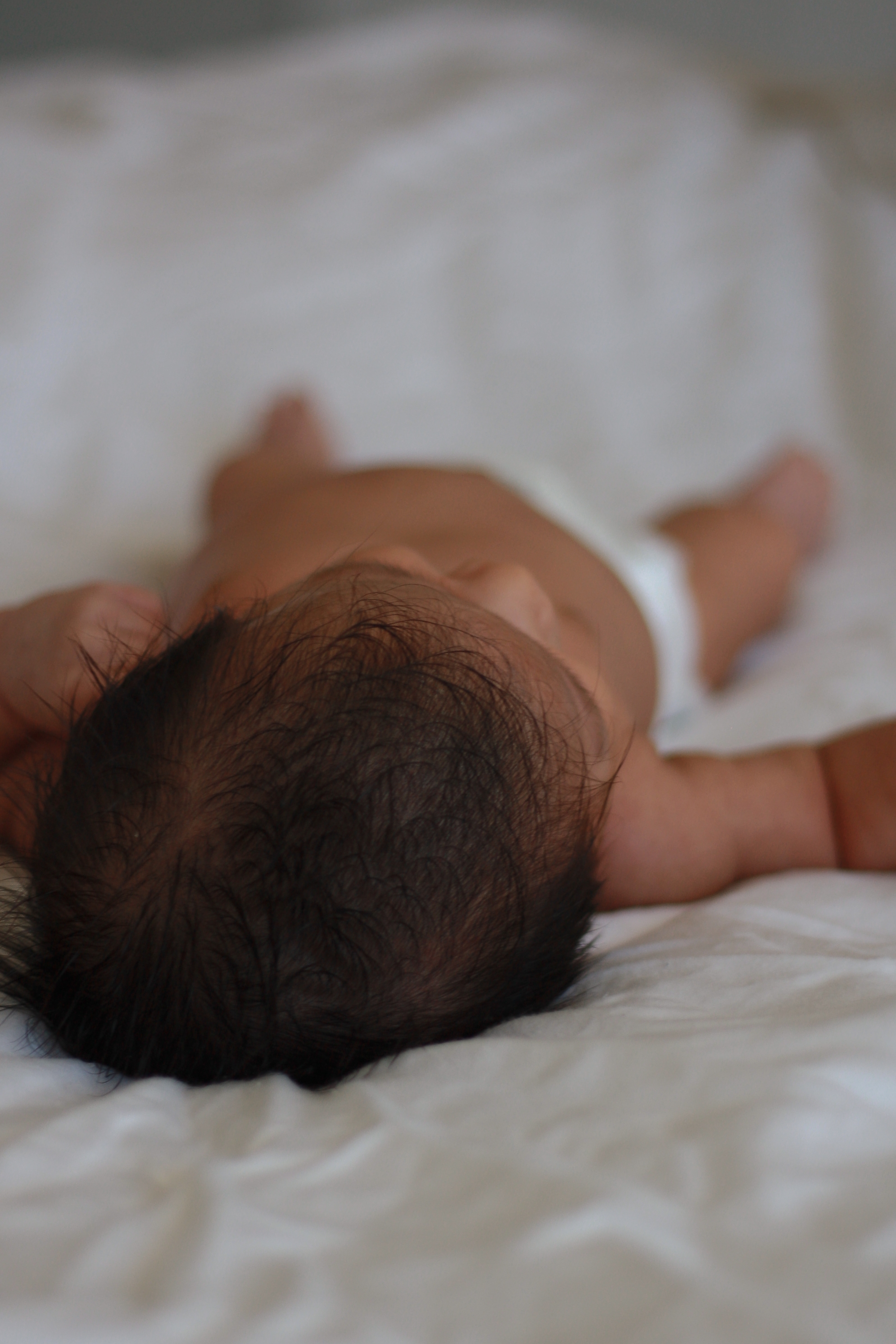 Top of newborn baby head perspective while baby lays on white sheets - Newborn Photography