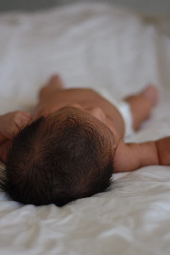 Top of newborn baby head perspective while baby lays on white sheets - Newborn Photography