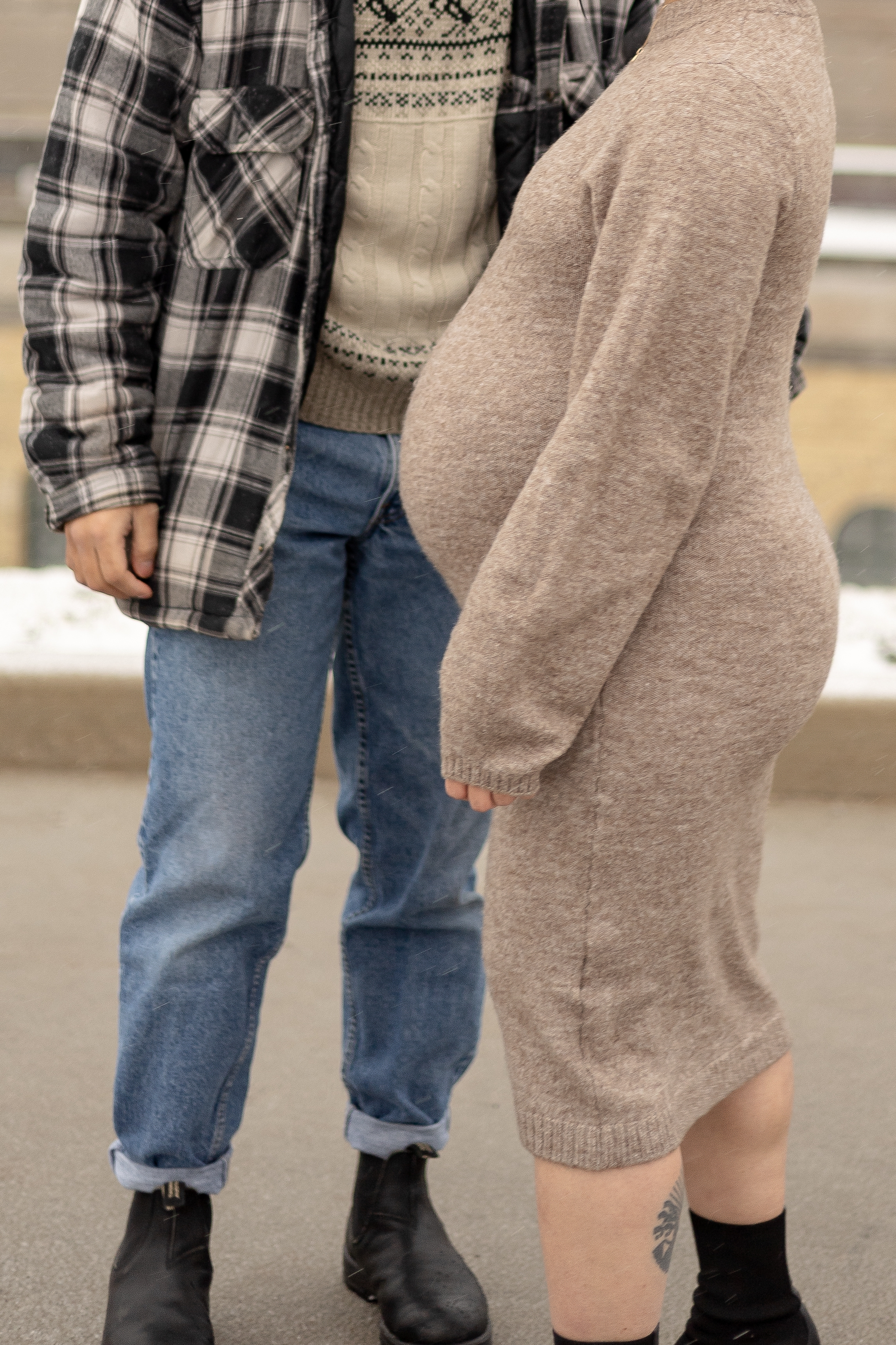 Close up winter maternity. Mom in brown knit dress facing left while dad stands behind her in flannel shirt and jeans - Toronto Maternity Photographer