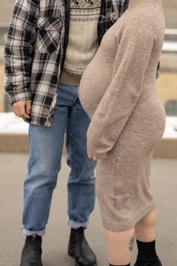 Close up winter maternity. Mom in brown knit dress facing left while dad stands behind her in flannel shirt and jeans - Toronto Maternity Photographer