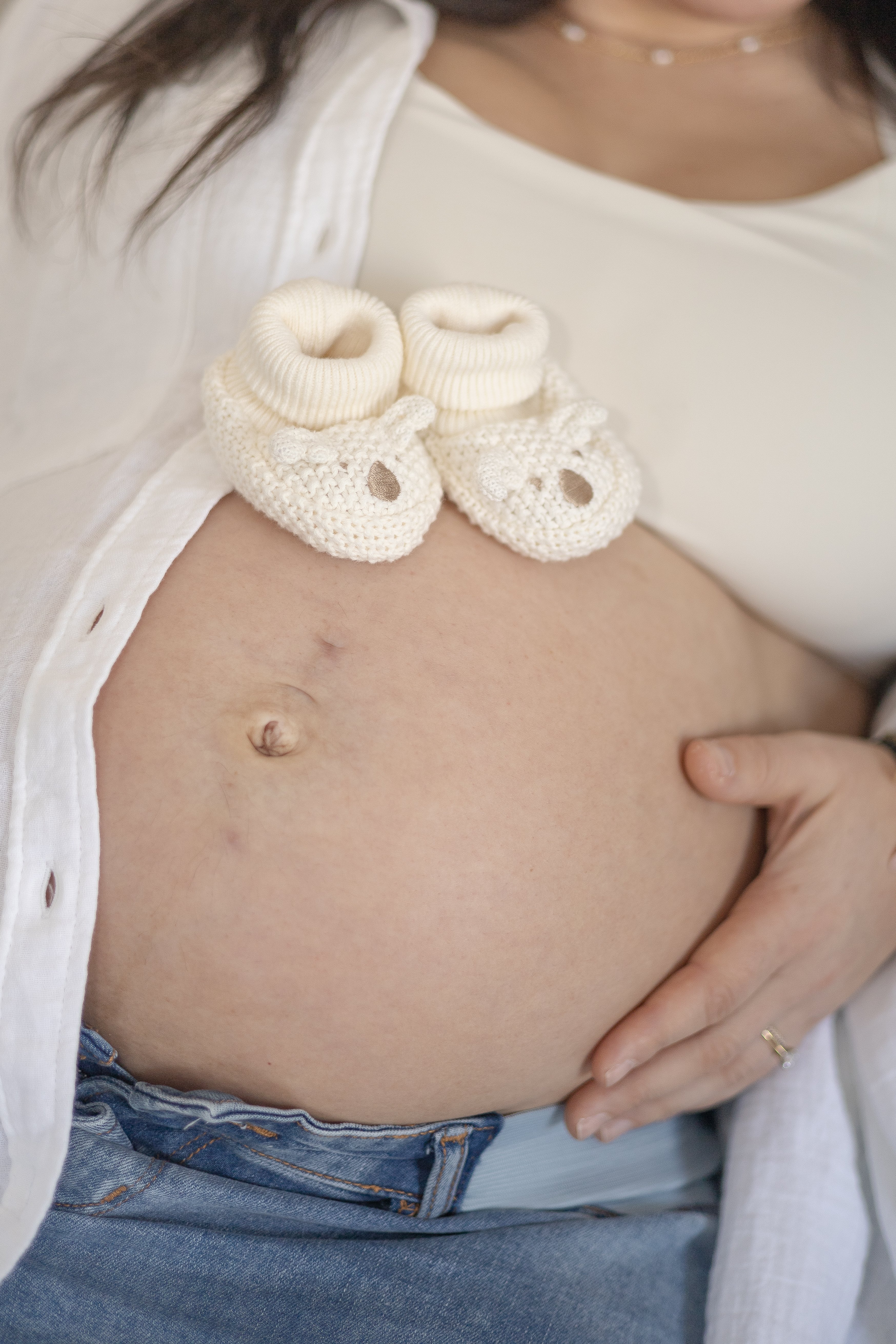 Close up of pregnant belly with knit baby shoes resting on it - Newmarket Maternity Photographer