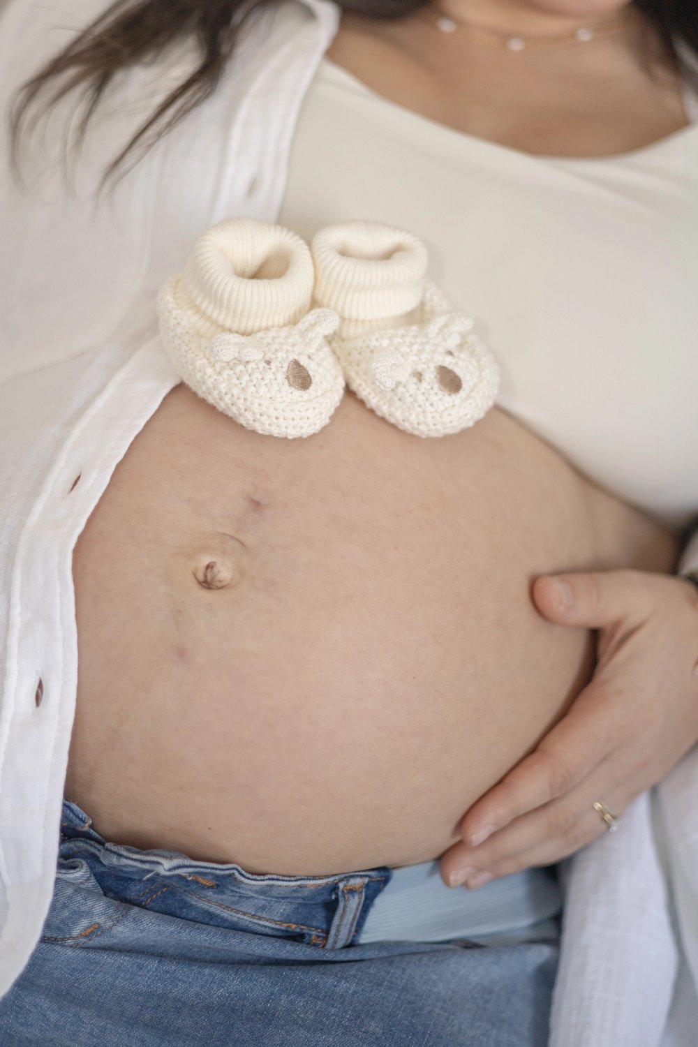 Close up of pregnant belly with knit baby shoes resting on it - Newmarket Maternity Photographer