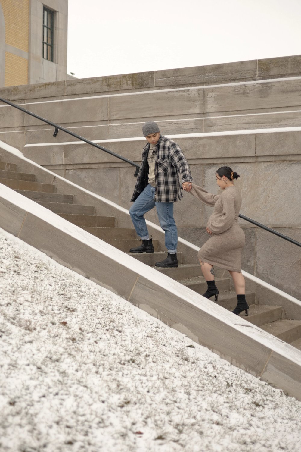 Natural moment maternity photo of an expectant mother walking up stairs near the iconic lakeside view at the R.C. Harris Water Treatment Plant while husband leads the way holding her hand. - Newmarket Maternity Photographer