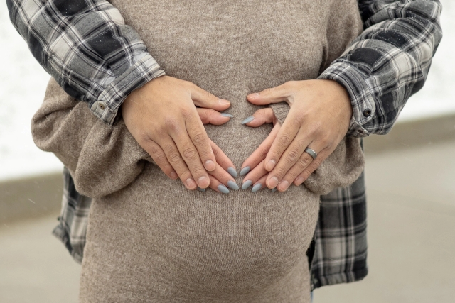 Close up of expectant parents making a heart with their hands over pregnant woman's baby bump.