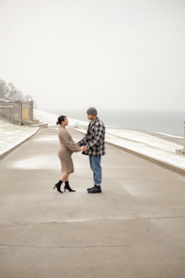 Pregnant mother and expecting father holding hands against the iconic lakeside view at the R.C. Harris Water Treatment Plant.