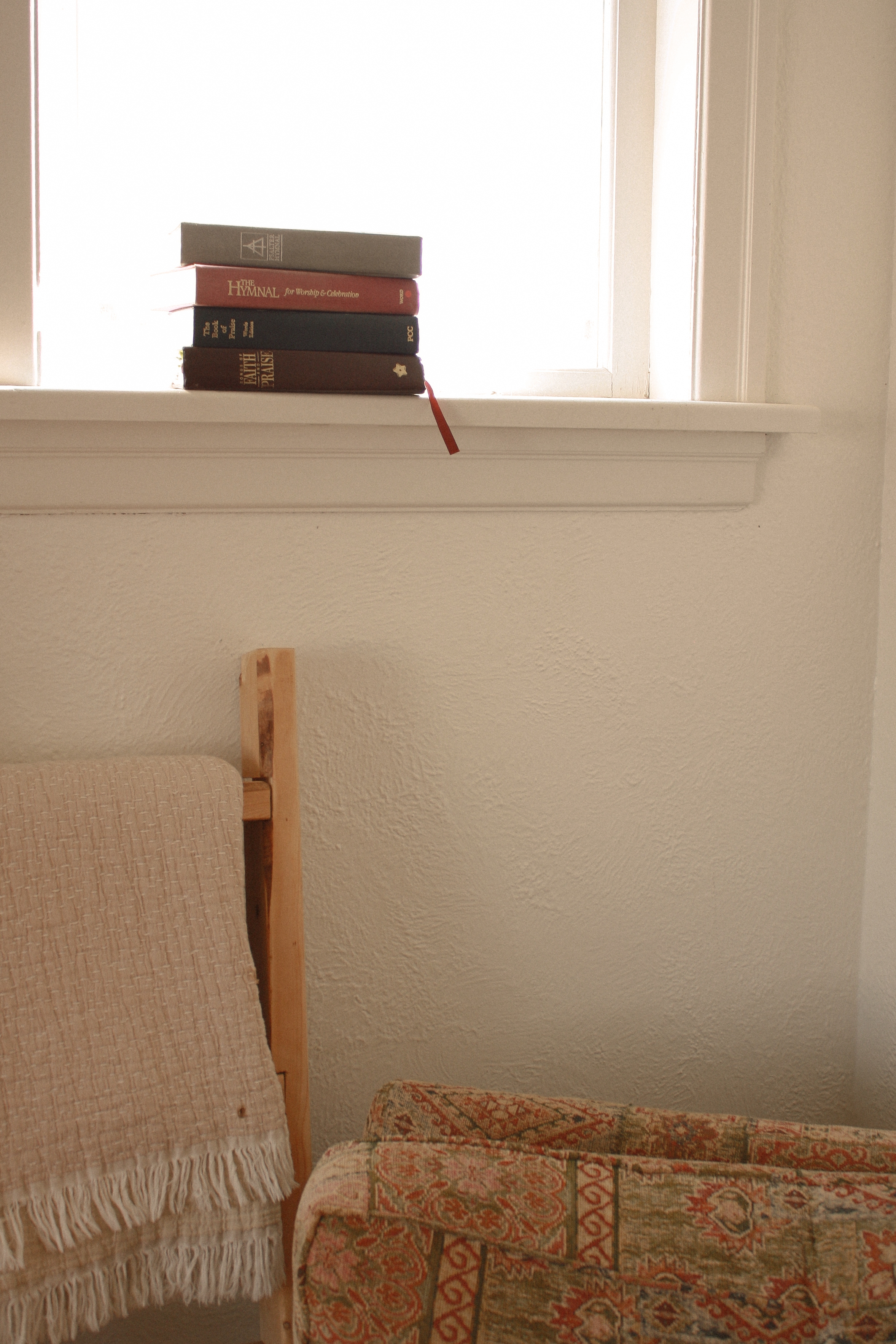 Hymn books stacked on window sil in family home above an arm chair and throw blanket - Family Photography