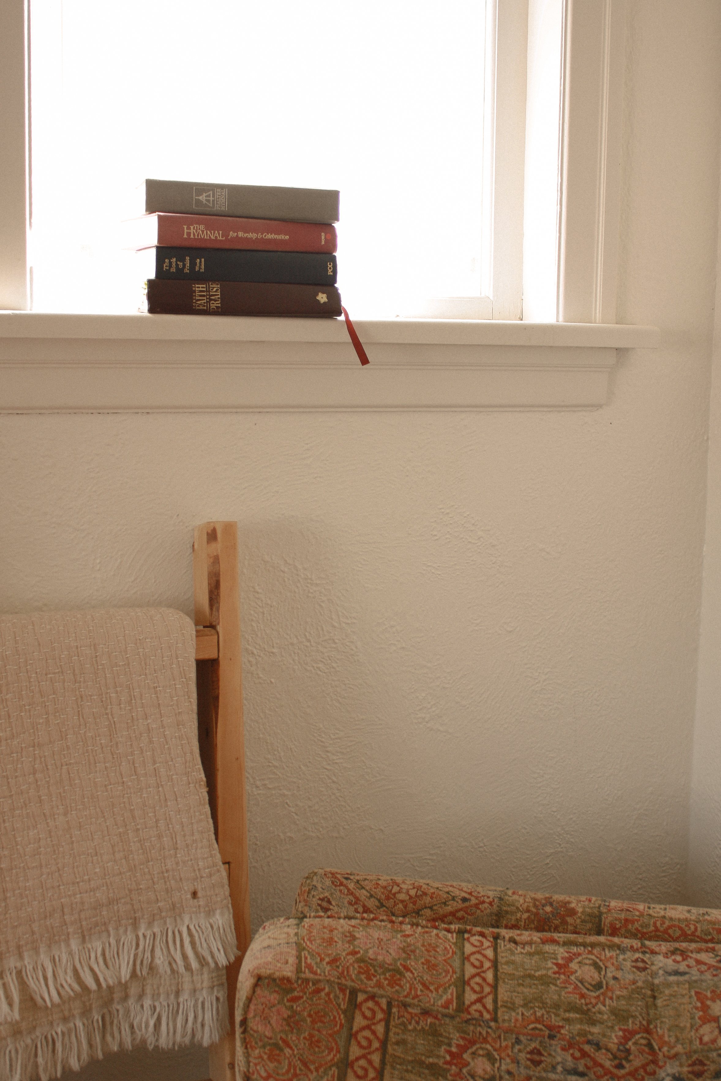 Hymn books stacked on window sil in family home above an arm chair and throw blanket - Newmarket Family Photography