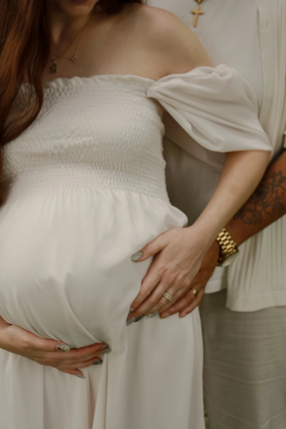 close up of woman in off the shoulder white dress holding her baby bump while husband stands behind her holding her hips - Newmarket Maternity Photography