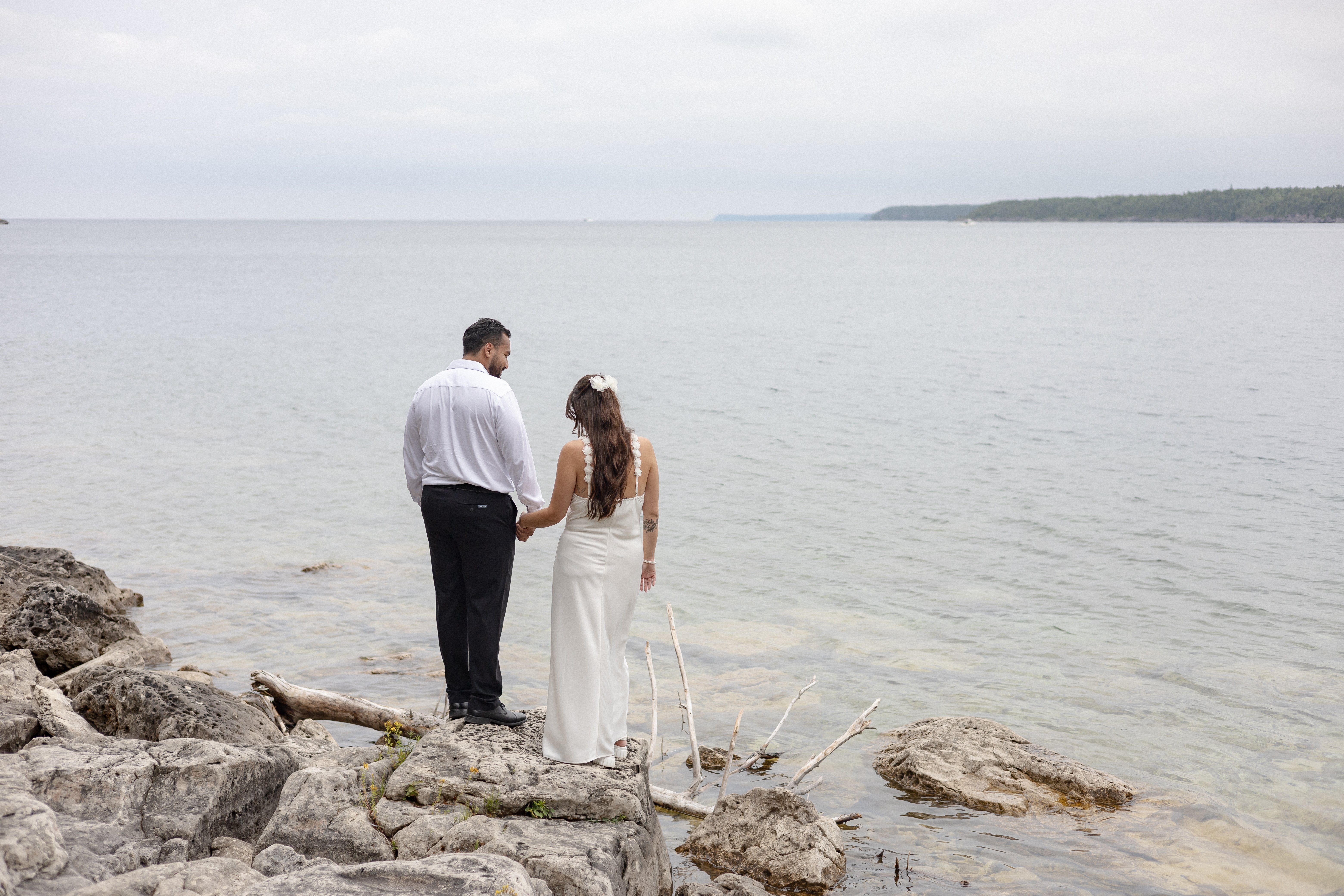 Bride and groom standing by rocks along a shoreline - Tobermory Elopement Photography