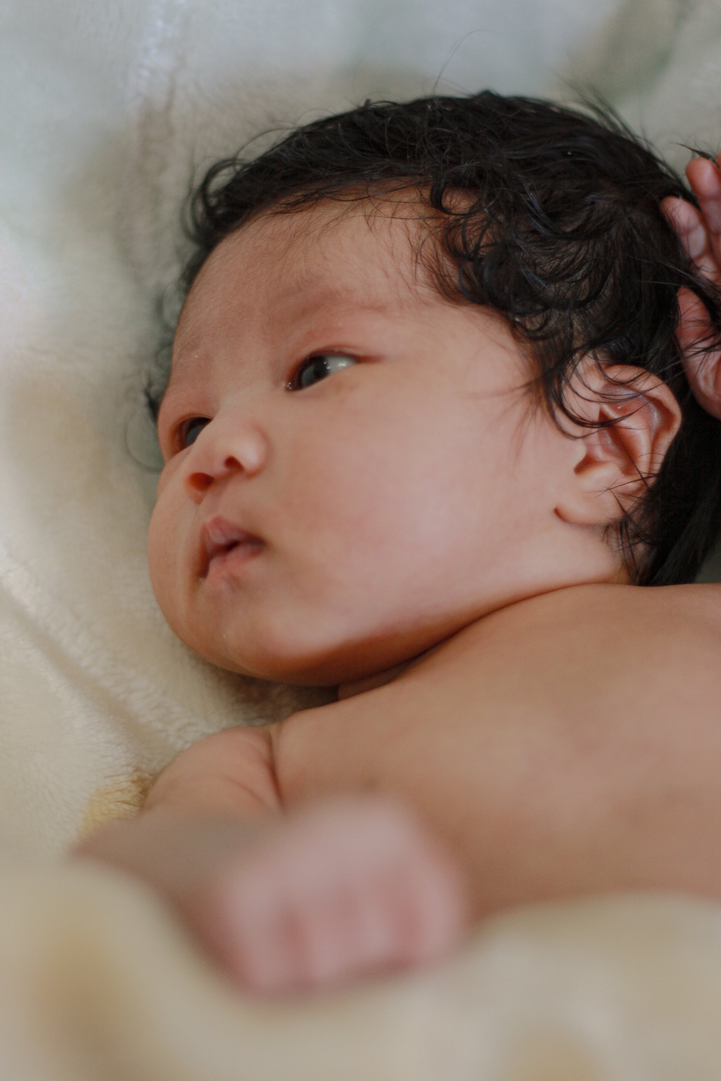 newborn baby with a lot of dark hair laying on white blanket looking to the left - Newmarket Newborn Photography