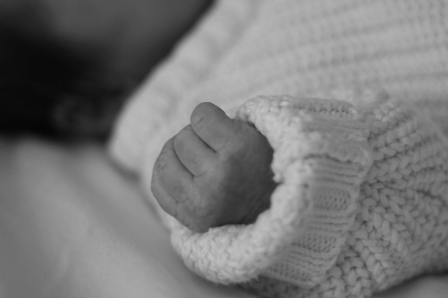 black & white close up of newborn hand while he is wearing a knit sweater - Newborn Photography