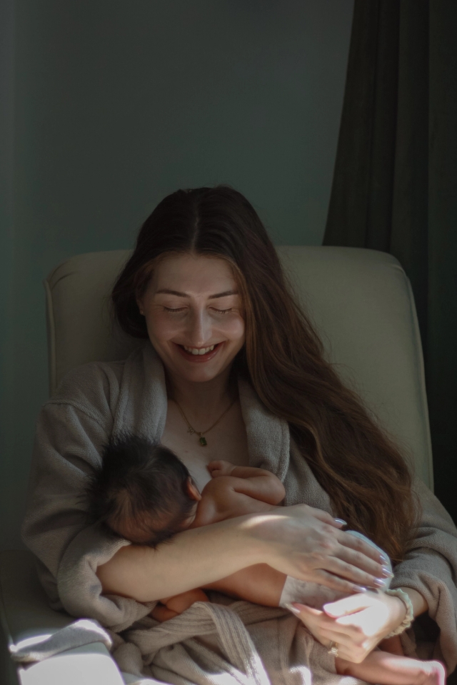 mom sitting in rocking chair smiling down at baby while nursing - newborn photography