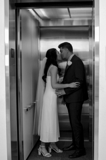 black and white photo of bride and groom standing in an elevator kissing - Wedding Photography