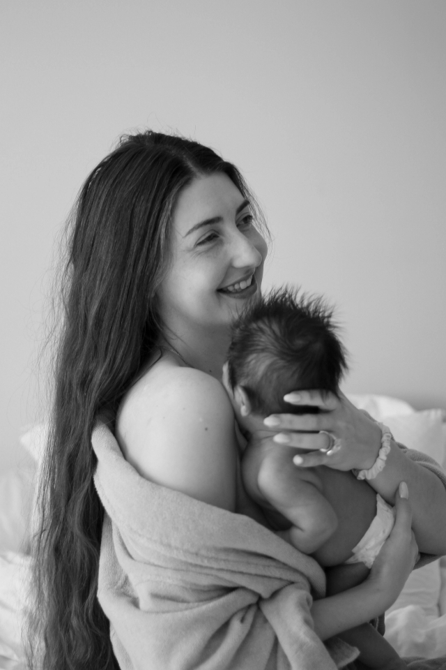 mom smiling while hugging newborn close to her while robe is falling off her shoulder - newborn photography