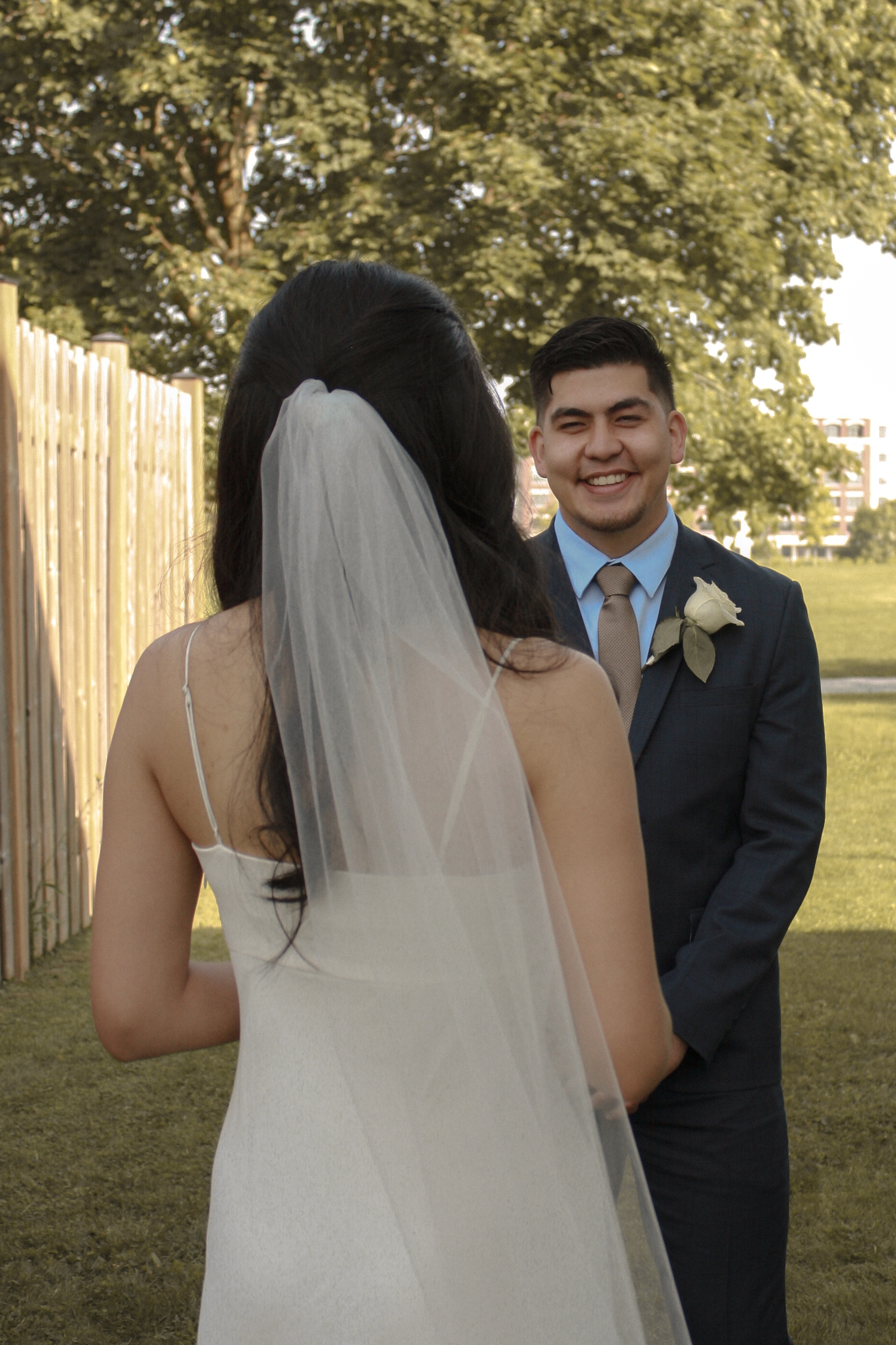 Bride and Groom doing first look, back of brides head with veil while groom is looking at her smiling with joy - Wedding Photography