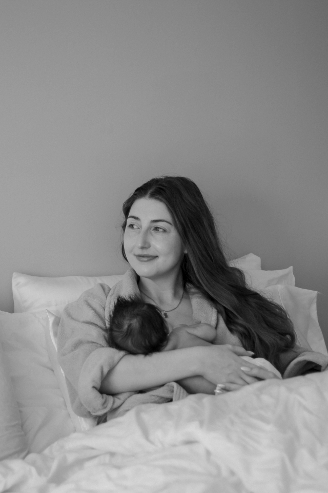 mom smiling and staring out the window while nursing baby - newborn photography