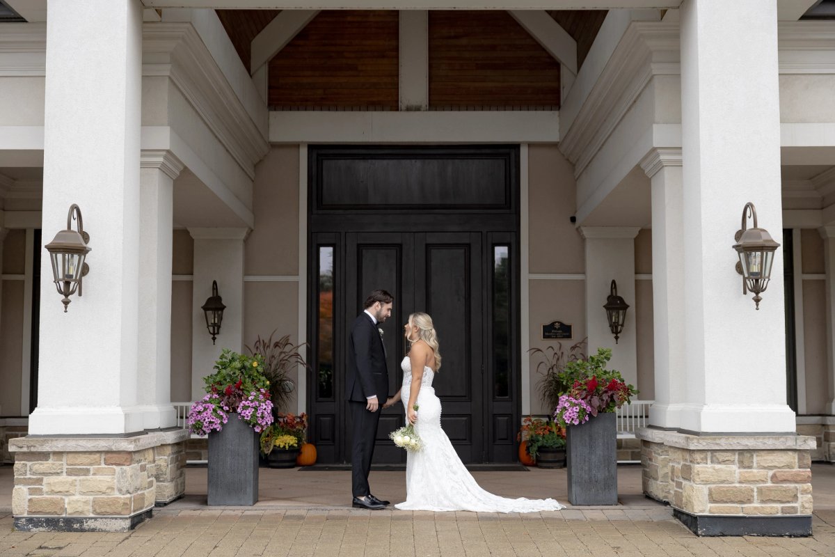 bride and groom holding hands facing each other in front of Barrie Country Club building