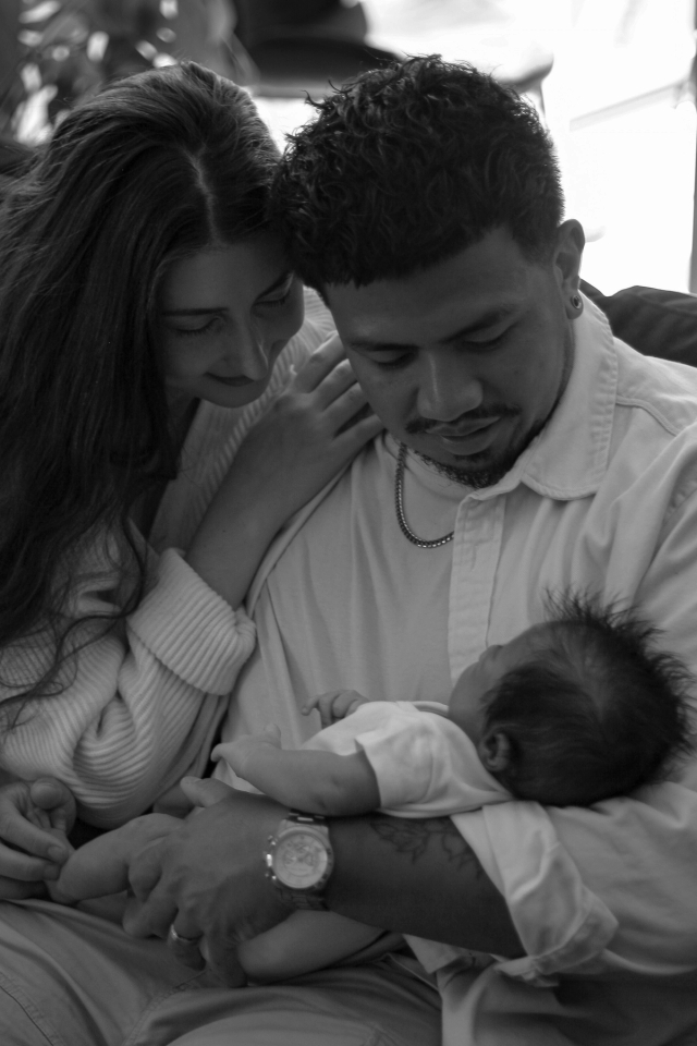 close up of parents sitting on couch admiring newborn baby in dad's arms, Black & White - Newborn Photography