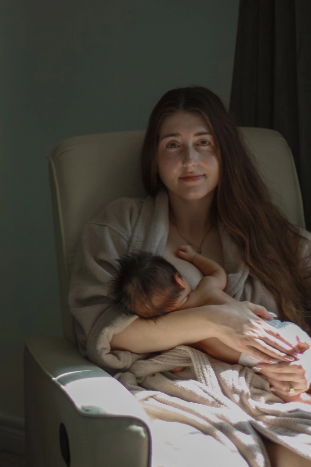 mom looking at camera while sitting in rocking chair nursing baby - newborn photography