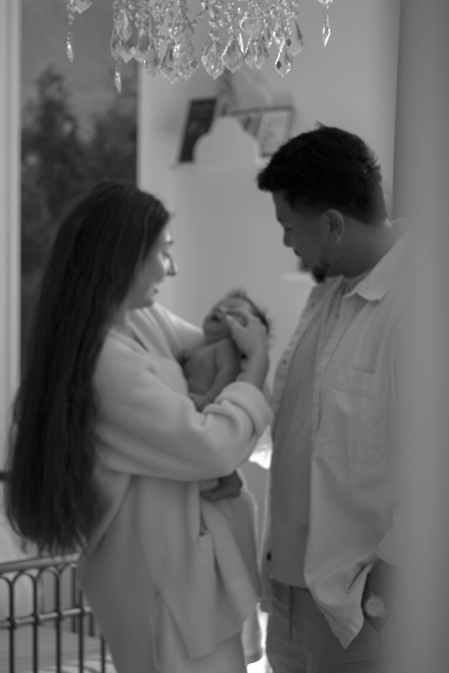 mom and dad standing in nursery under chandelier while mom is holding baby - newborn photography