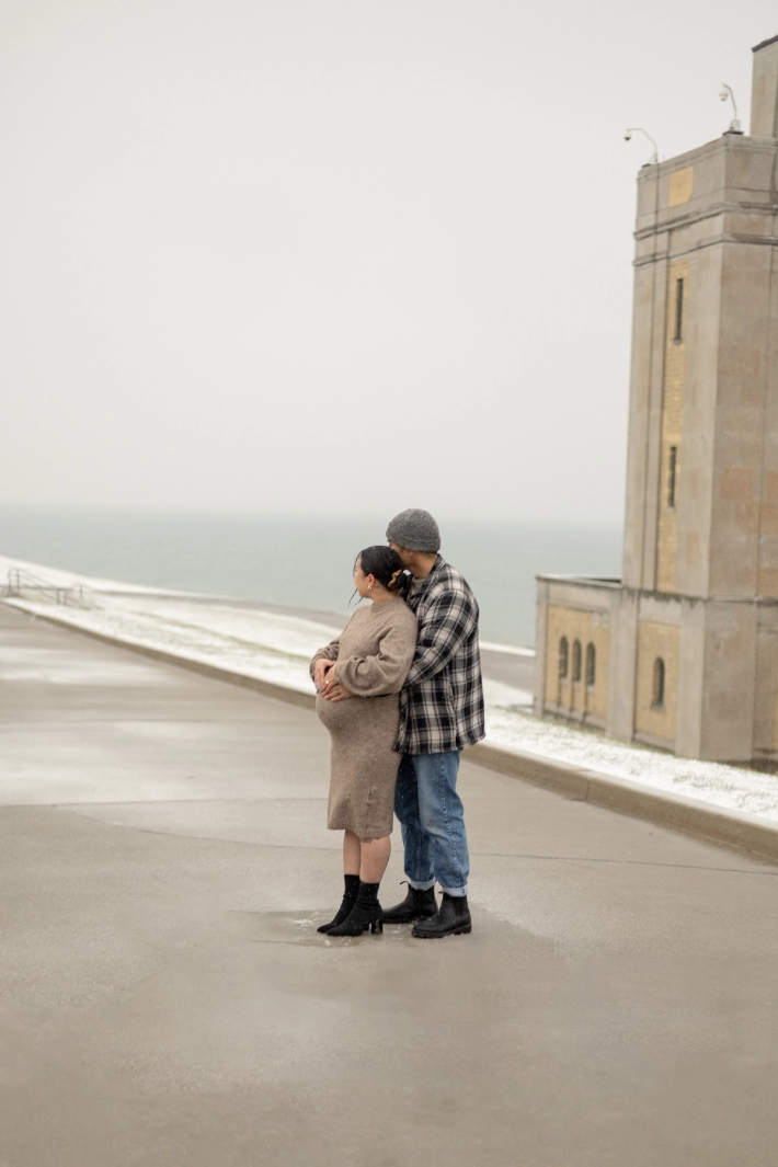 Documentary-style maternity photo of a woman and her husband cradling her baby bump in front of the historic Art Deco architecture in the GTA.