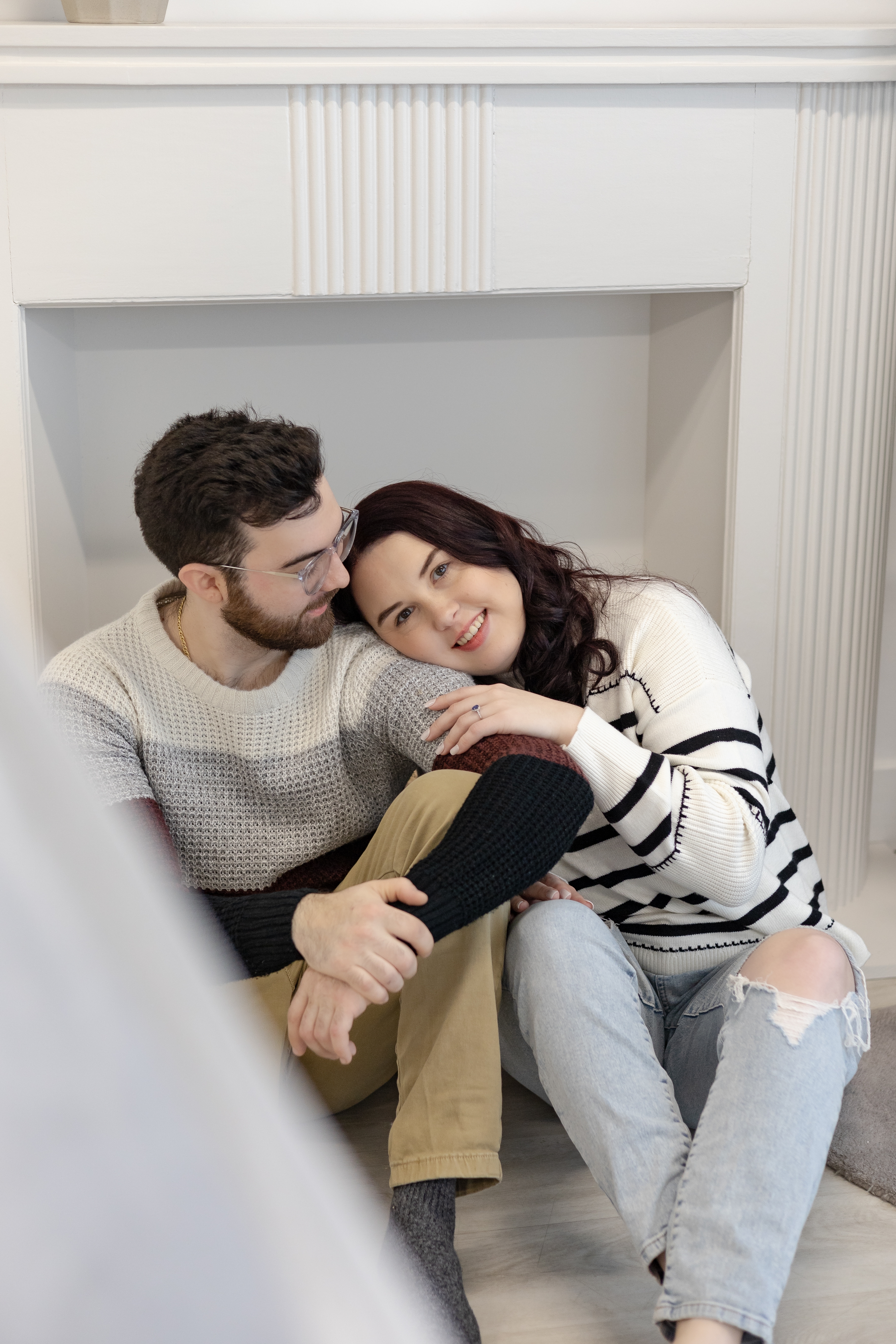 Couple sitting in front of fireplace cuddling in studio engagement photos