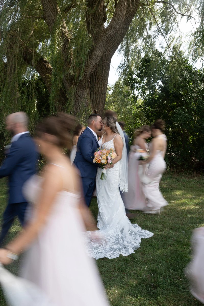 Bride and Groom kissing while wedding party walks past at Andrew's Tree Farm in Ancaster, Ontario
