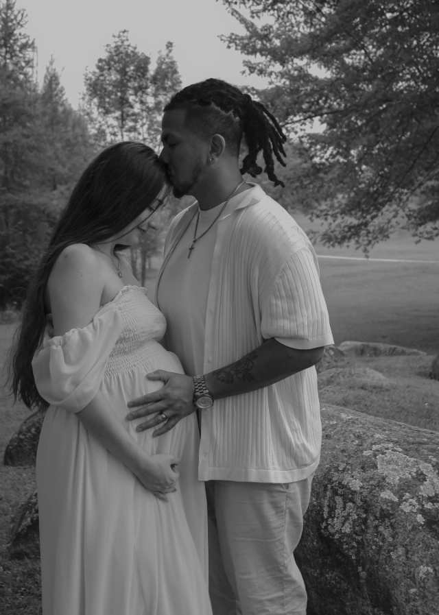 mom and dad standing holding baby bump while dad gives mom a kiss on the forehead - Maternity photography