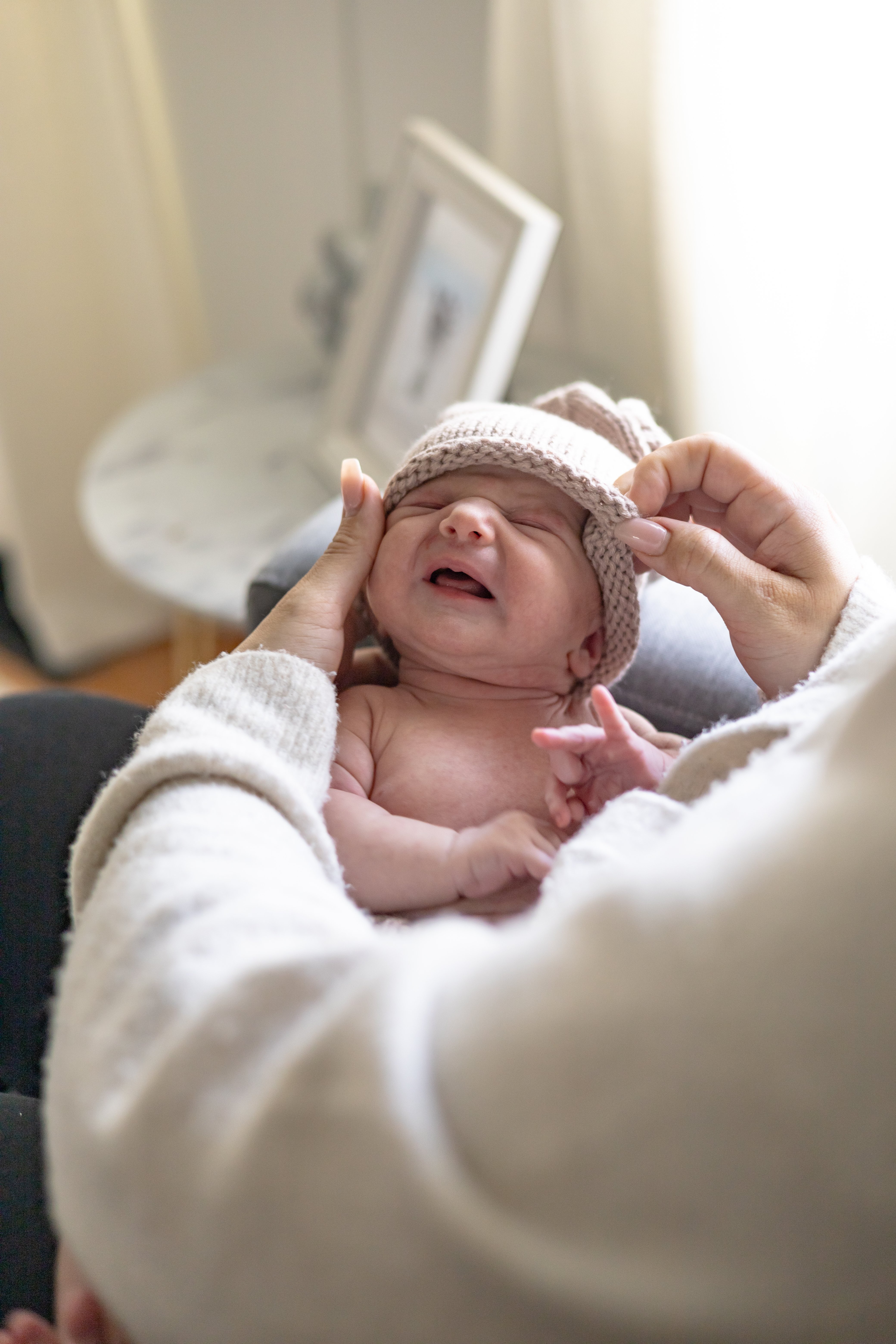 mom putting knit cap on newborn baby during in home newborn photoshoot in Newmarket, Ontario