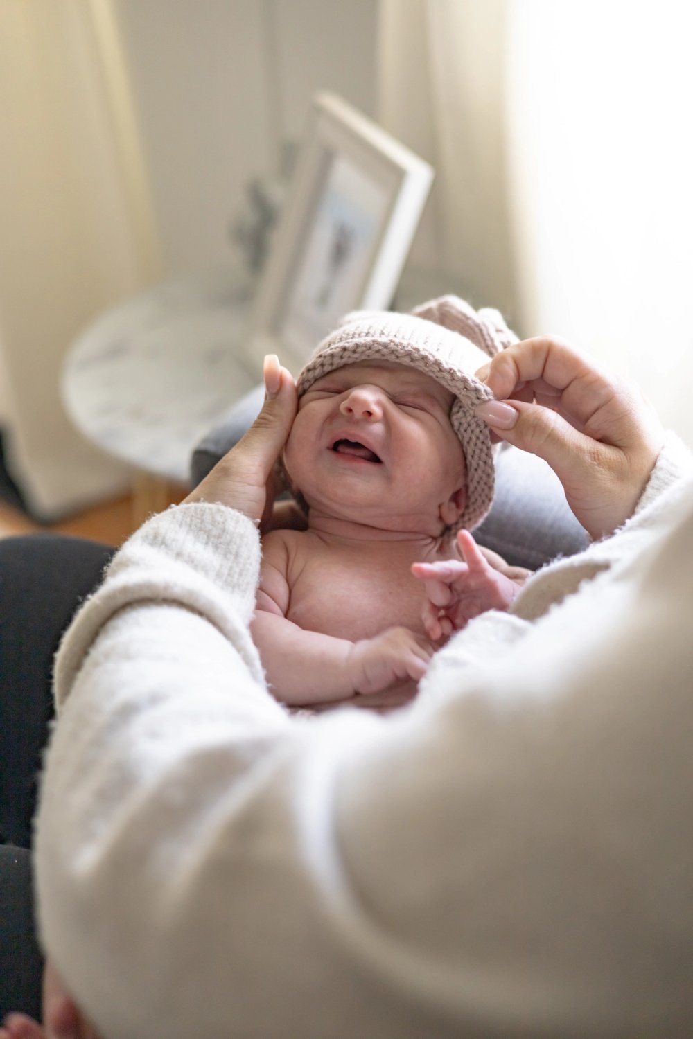 mom putting knit cap on newborn baby during in home newborn photoshoot in Newmarket, Ontario
