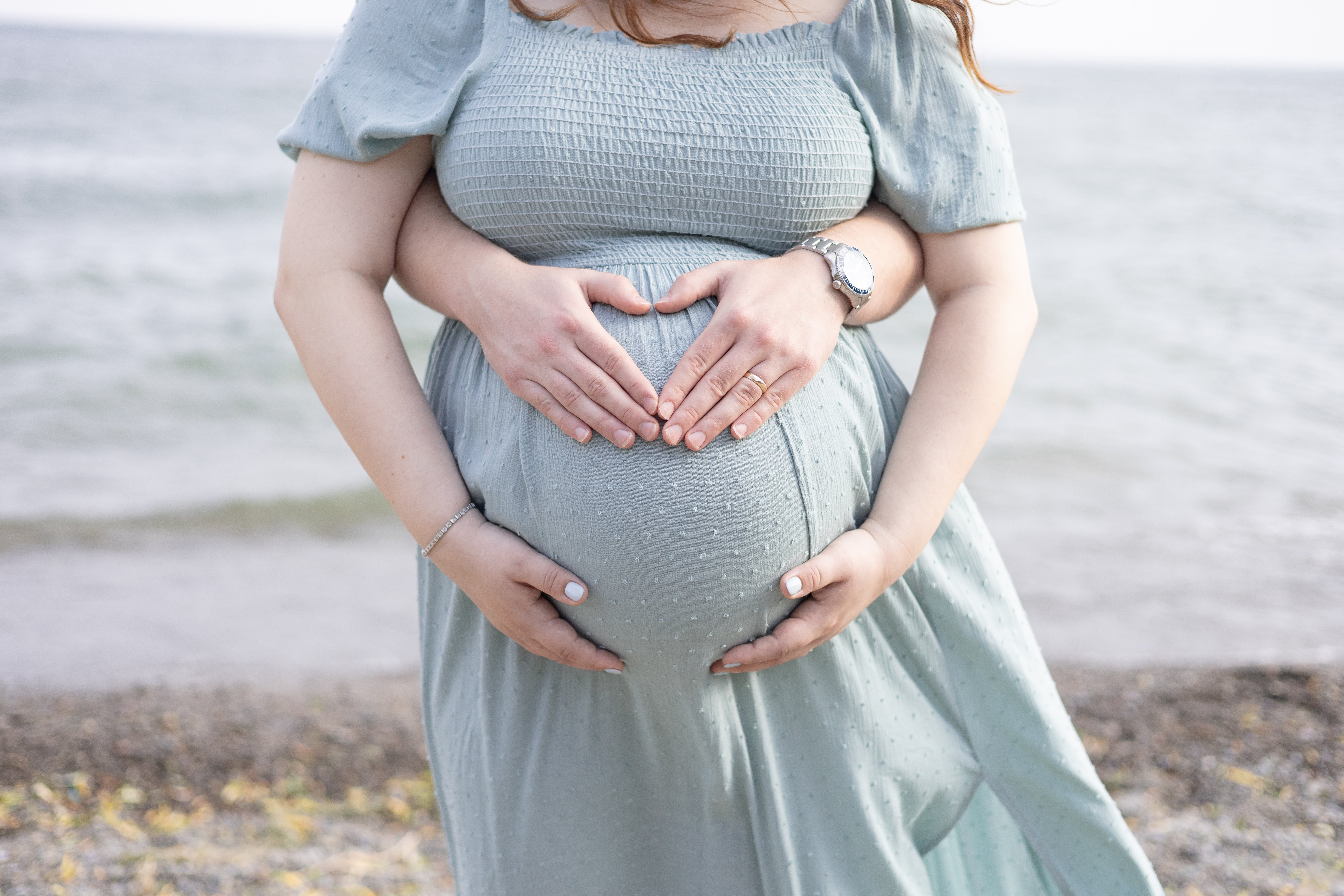 Close up of mom and dad holding baby bump at an Ontario beach