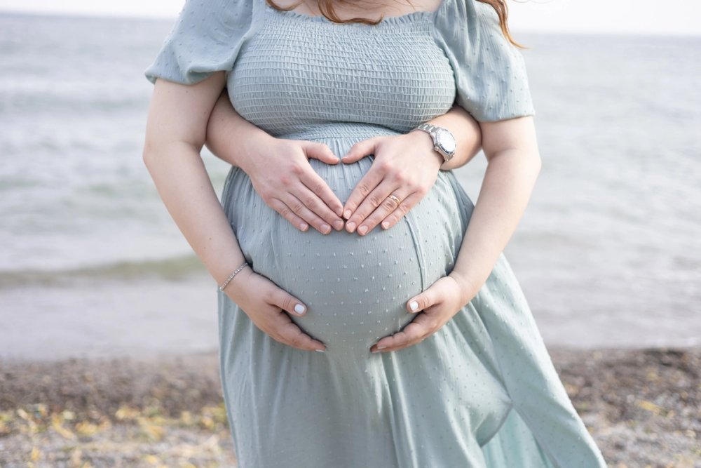 Close up of mom and dad holding baby bump at an Ontario beach
