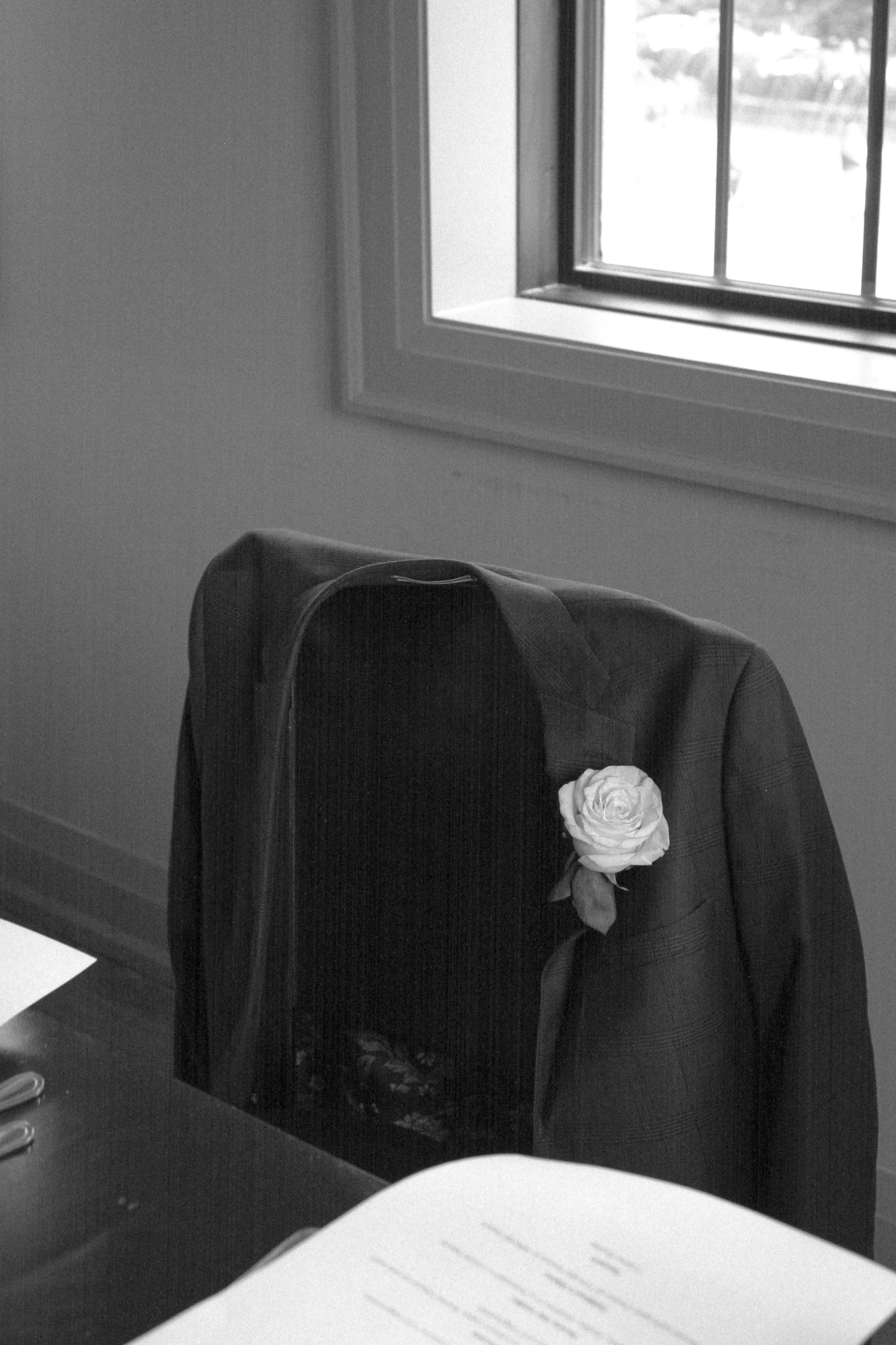 black and white image of Grooms suit jacket with white rose boutonniere resting on chair at wedding reception - Elopement Photography