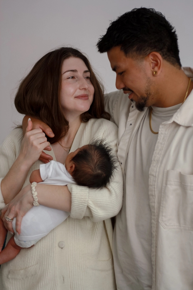 parents standing looking at each other, dad has his arm around mom while she is holding baby and his hand - Newborn photography