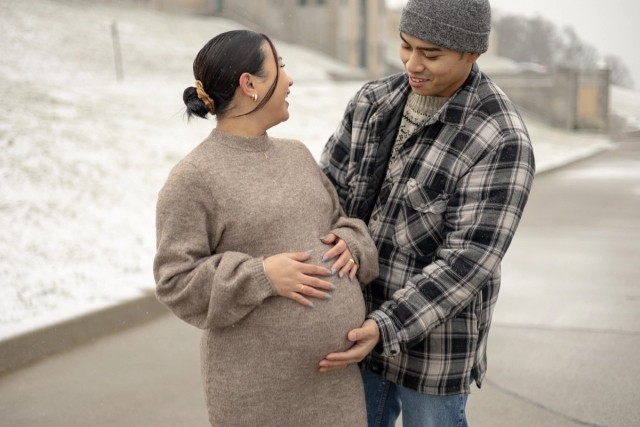 Expectant parents holding baby bump while looking at each other laughing during a winter maternity photoshoot in Scarborough, Ontario.