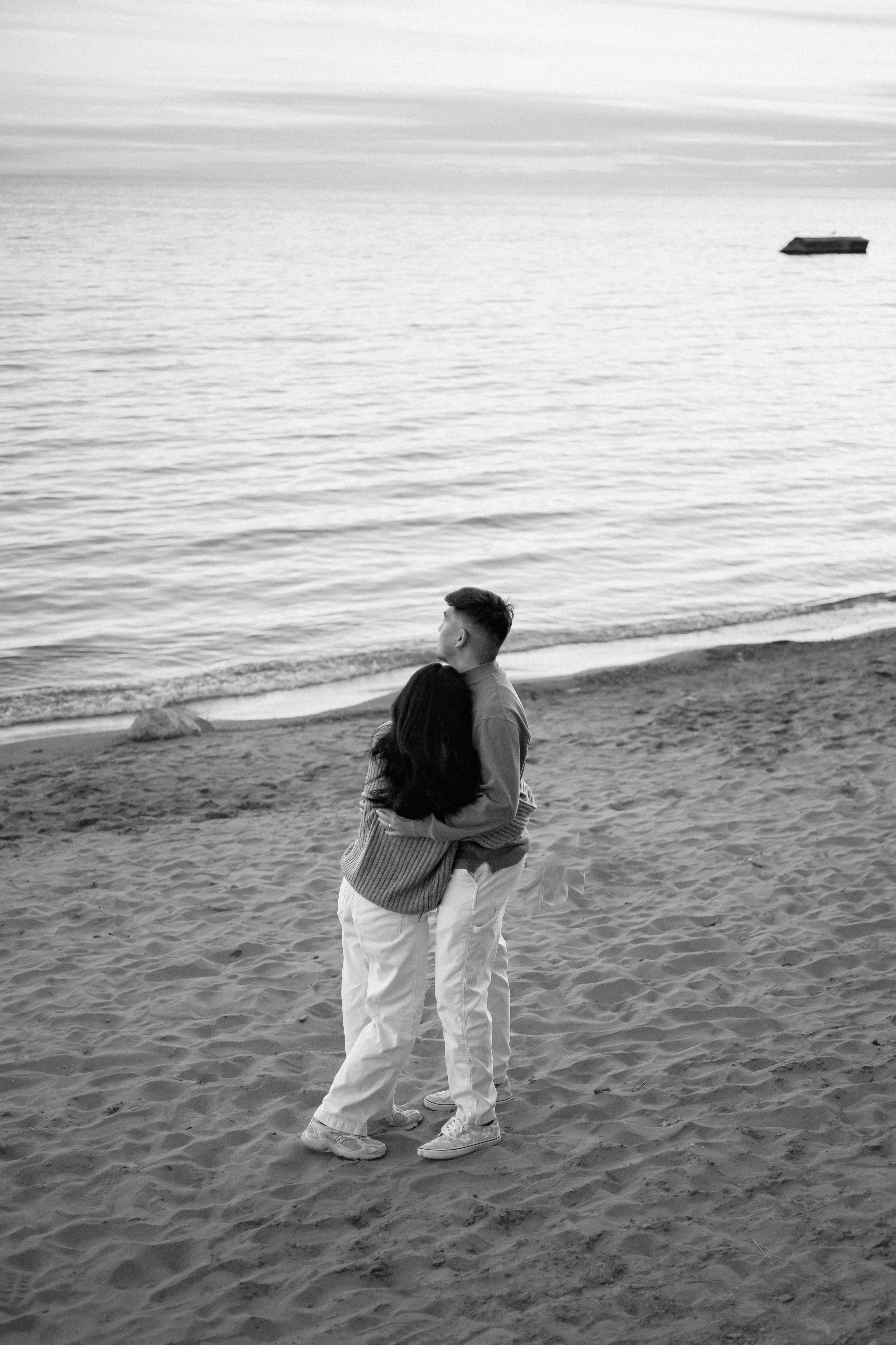 couple standing on beach in front of water, hugging - Portrait Photography