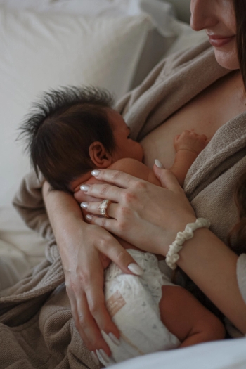 Mom breastfeeding newborn baby in robe while smiling, wearing engagement ring and scrunchie on wrist - Newborn Photography