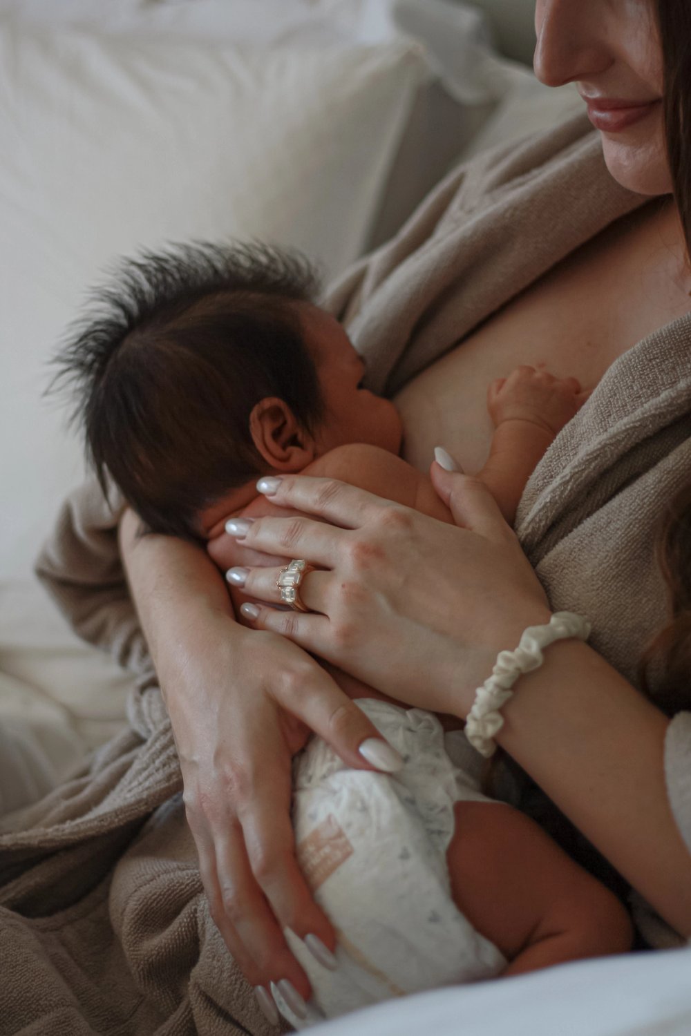 Mom breastfeeding newborn baby in robe while smiling, wearing engagement ring and scrunchie on wrist - Newmarket Newborn Photography