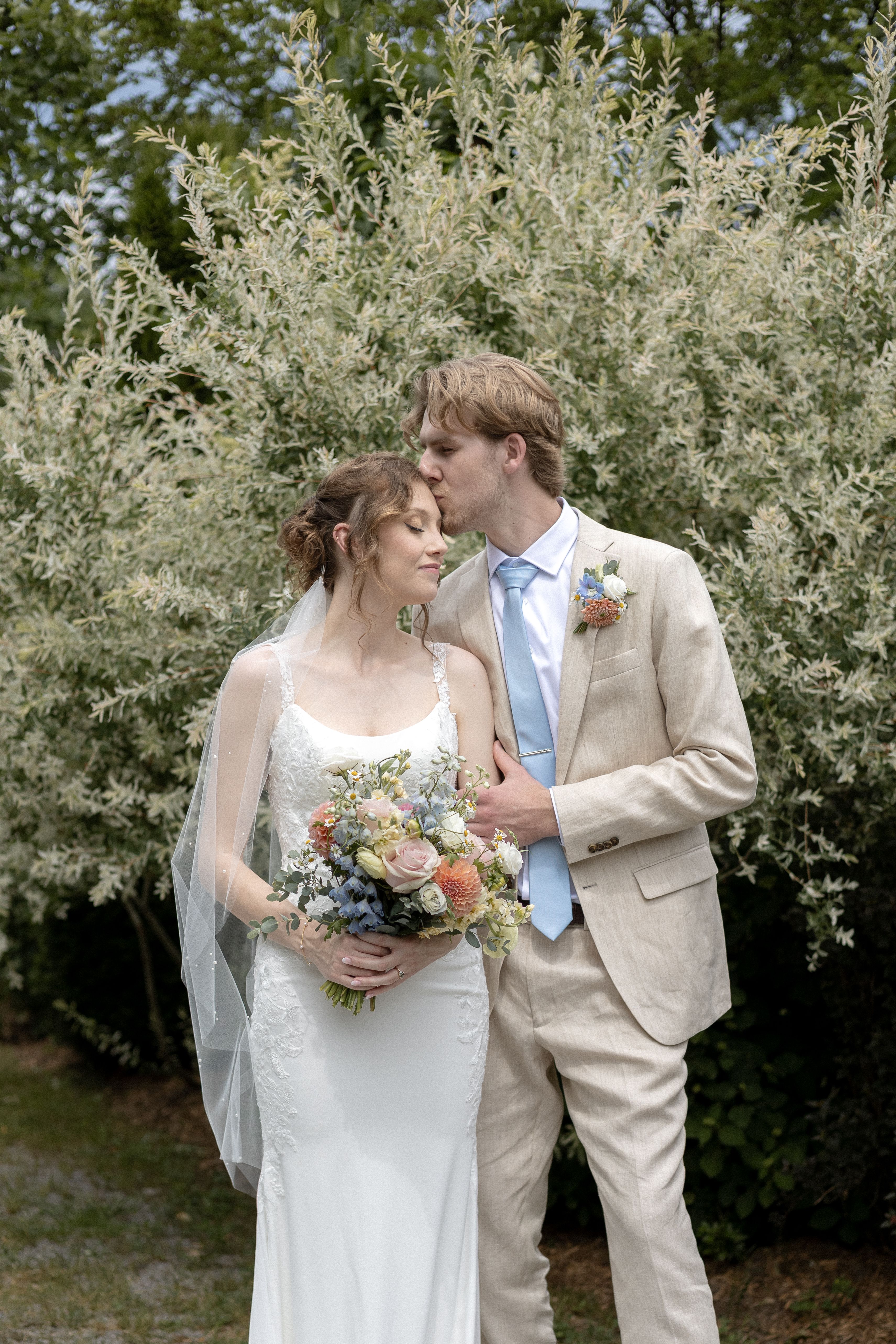 First look portrait of groom kissing bride's forehead