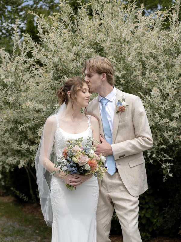 First look portrait of groom kissing bride's forehead