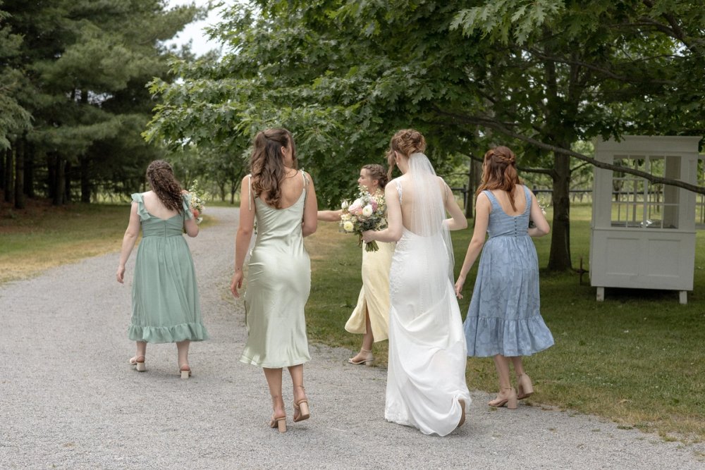 wedding party in colourful dresses walking down gravel path after wedding ceremony