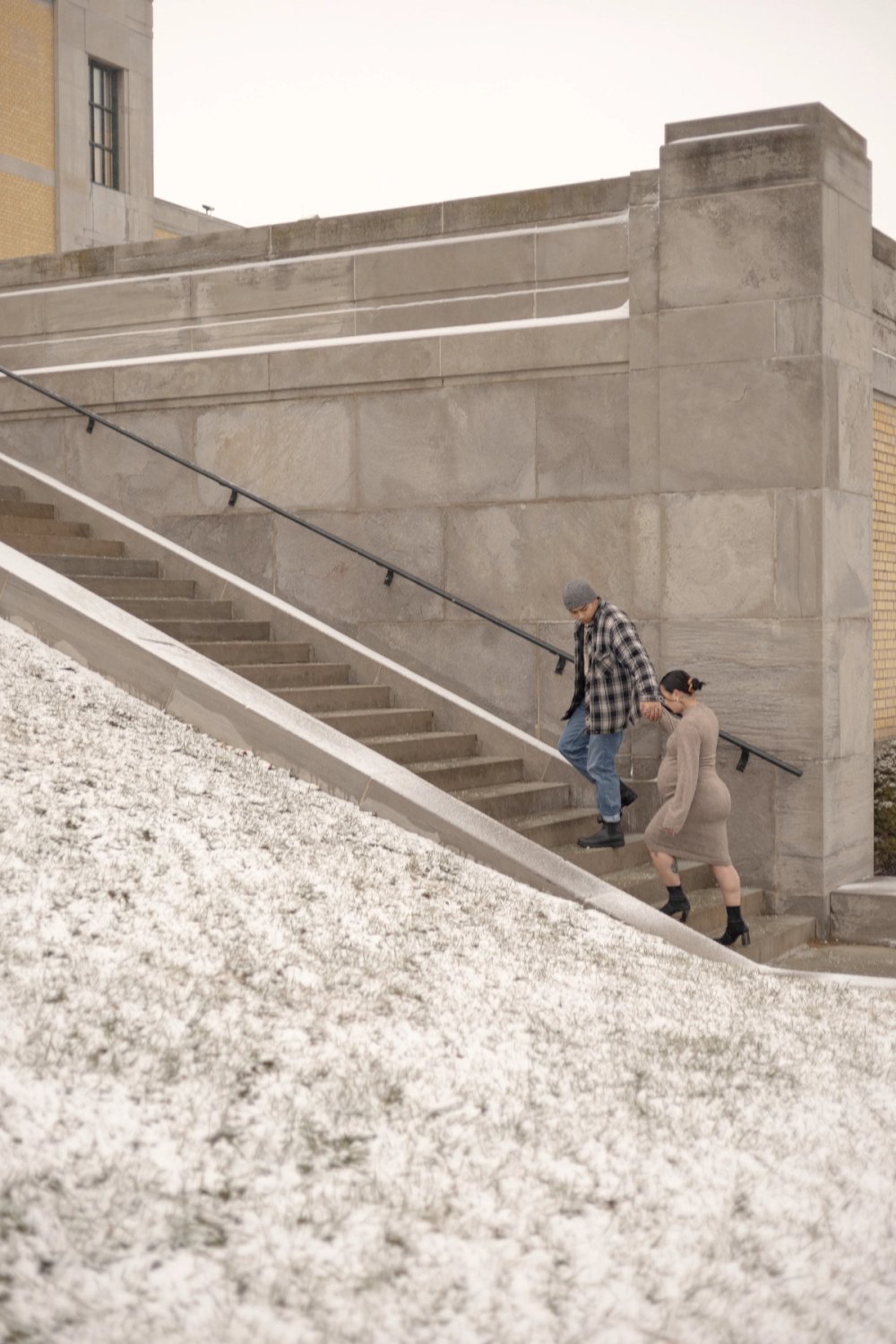 Natural moment maternity photo of an expectant mother walking up stairs near the iconic lakeside view at the R.C. Harris Water Treatment Plant while husband leads the way holding her hand. - Newmarket Maternity Photography