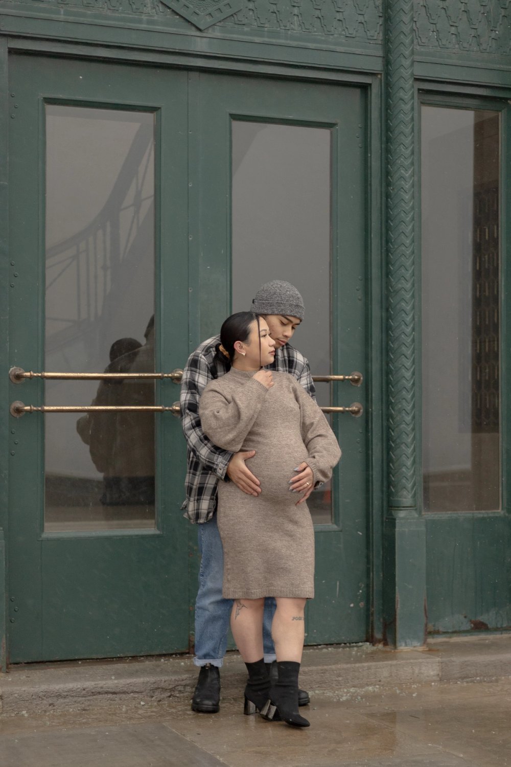 Couple standing in front of green door, dad behind mom holding her belly - Newmarket Maternity Photography